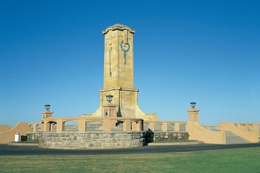 A tall, beige tower with a clock, surrounded by a stone wall and lamp posts. 4