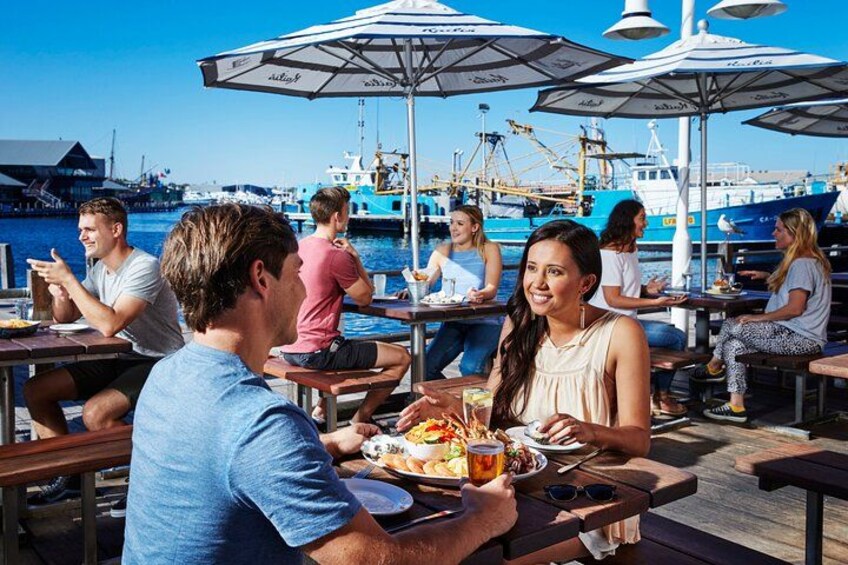 People dining at an outdoor restaurant with a marina in the background. 2