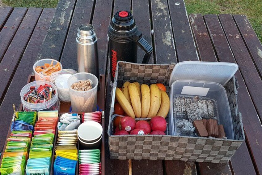 A picnic setup with food items, a thermos, and a cooler on a wooden table. 2