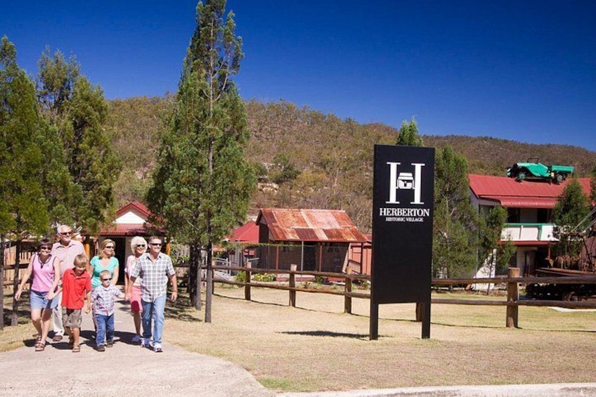 Eine Gruppe von Personen steht vor einem Schild mit der Aufschrift 'Herberton Historic Village'. 1