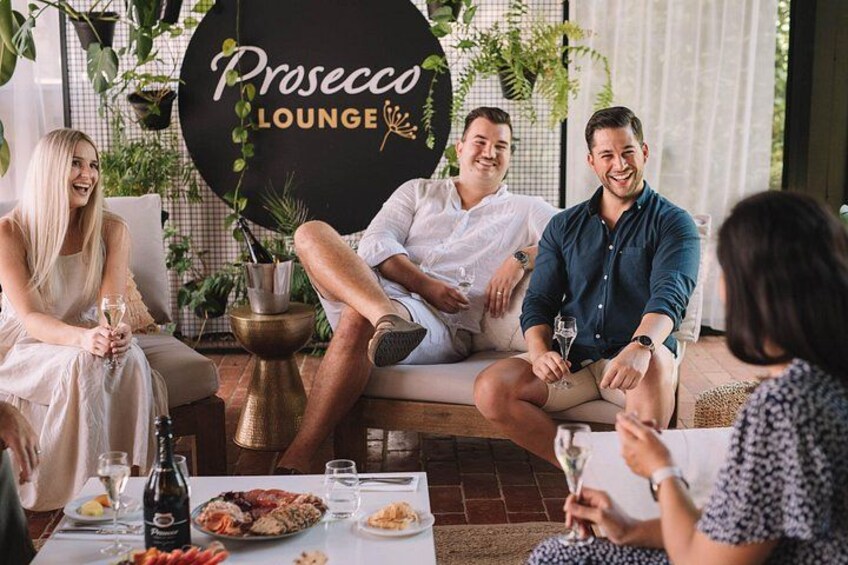 Un groupe de personnes est assis et discute dans un salon où est affiché un panneau indiquant : « Salon Prosecco ». 2