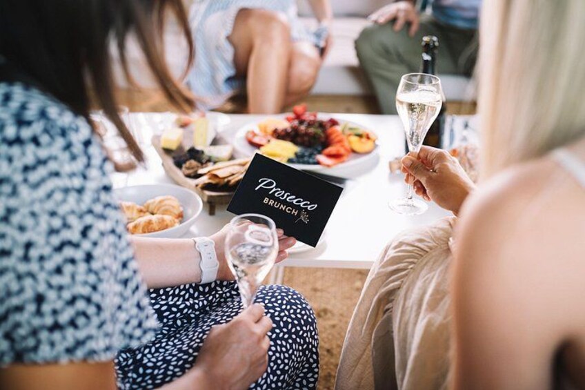 Une table dressée pour un brunch, avec des personnes assises, tenant des menus et des verres de vin. 4