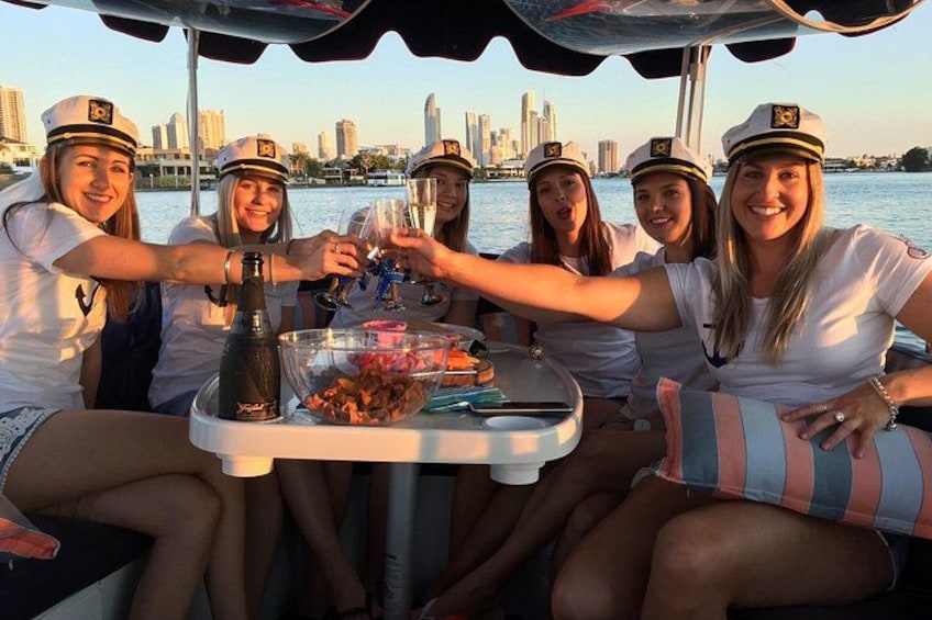 A group of people in sailor uniforms toasting with champagne on a boat with a city skyline in the background. 5