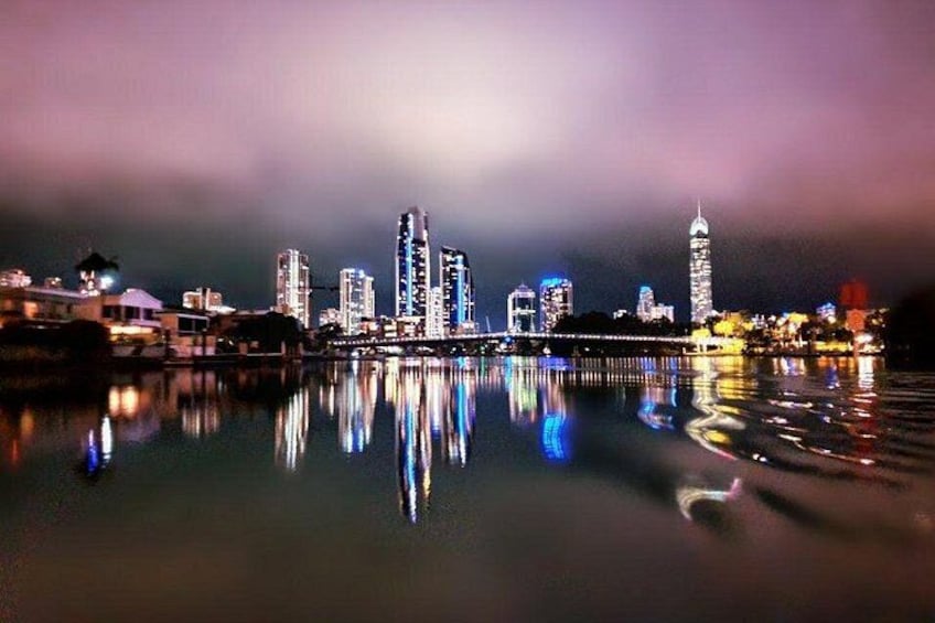 A nighttime cityscape with illuminated buildings reflected in calm water. 4