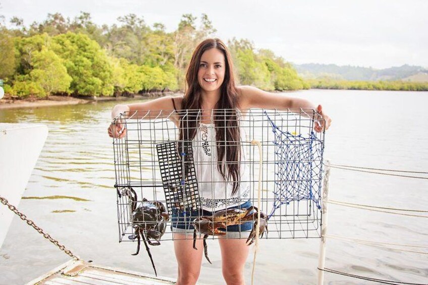 A person holding a wire cage with a fish inside, standing on a dock by a body of water with trees in the background. 1