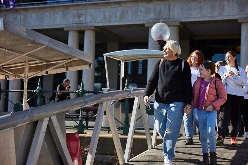 A pedestrian walkway with a metal structure, a person walking, and a group of people in the background. 4