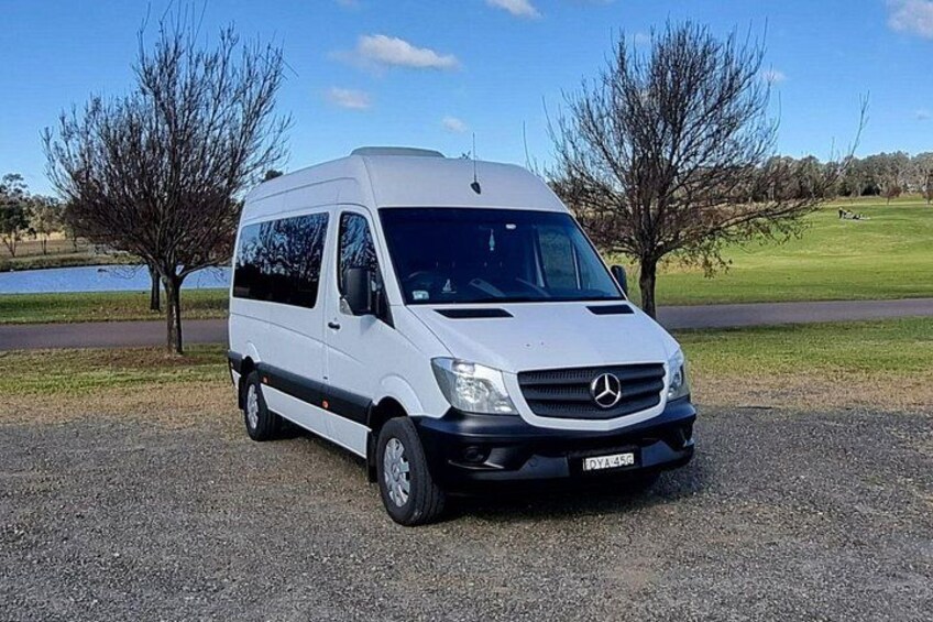En hvid Mercedes varevogn parkeret på en grusvej med træer og et vandareal i baggrunden. 3