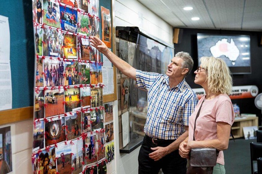 A man pointing at a wall covered with photographs. 2