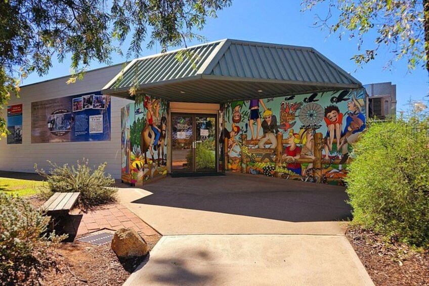 A building with a mural, a metal roof, and a paved entrance. 1