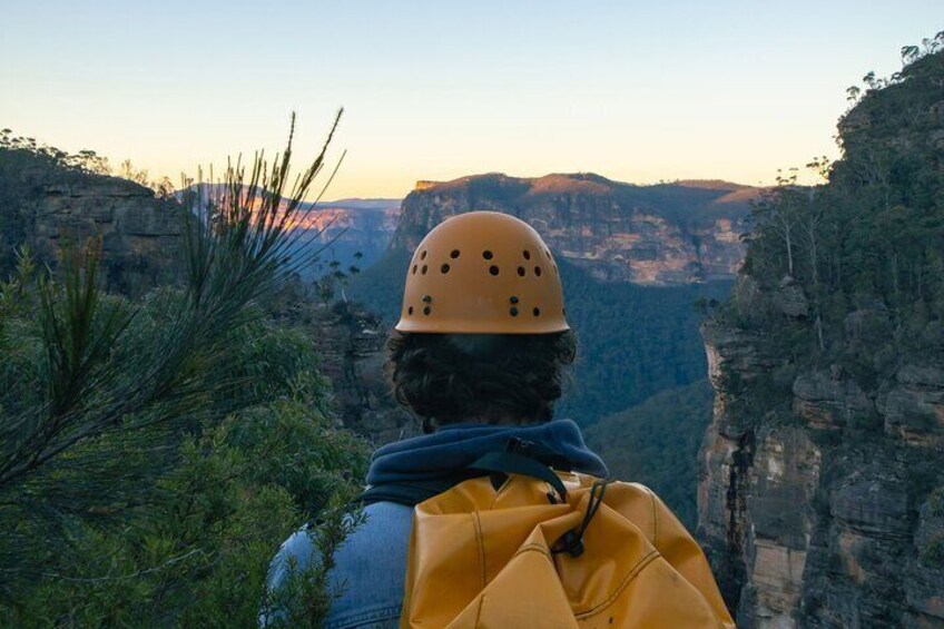 A person wearing a helmet and carrying a backpack, overlooking a canyon with steep cliffs and sparse vegetation. 2