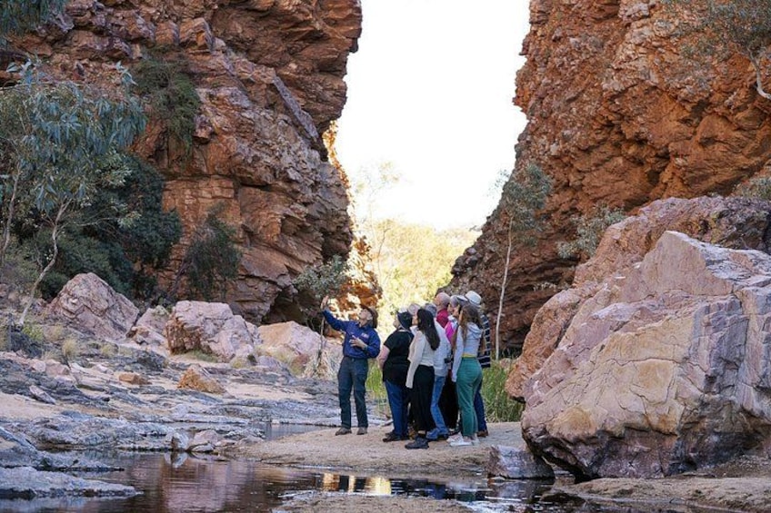 A group of people standing in a rocky canyon with a small water body in the foreground. 1