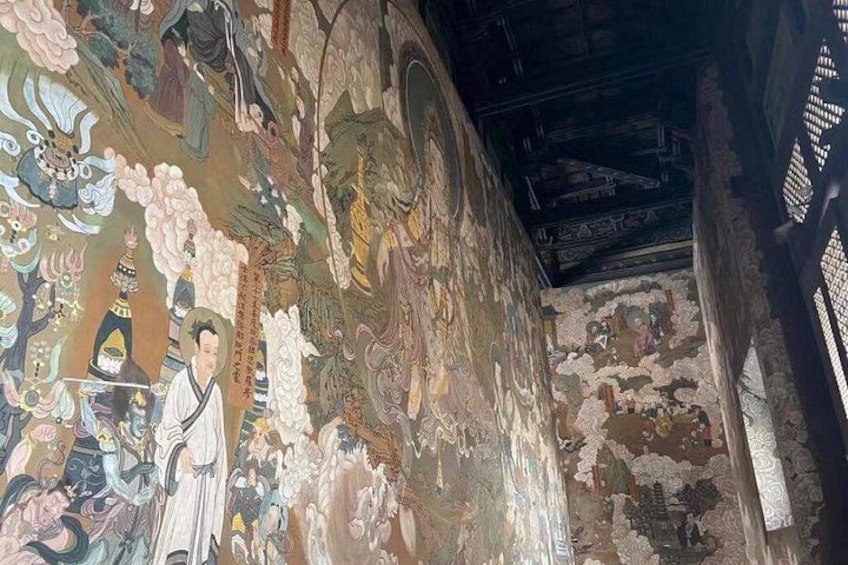 Een muurschildering met traditionele figuren en patronen, een houten plafond en een gedeeltelijk zichtbare muur. 4
