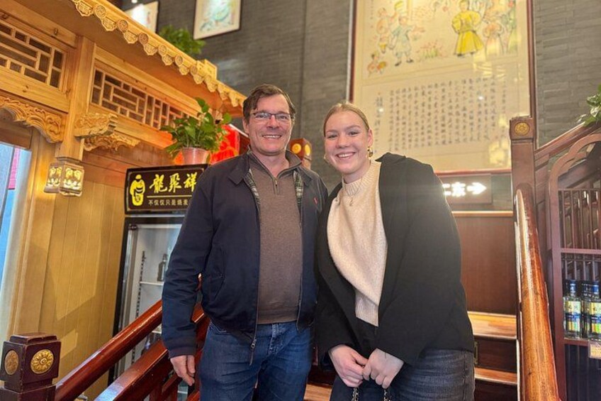 Een man en een vrouw staan in een restaurant met houten inrichting en een bord waarop 'Dragonfly' staat. 2