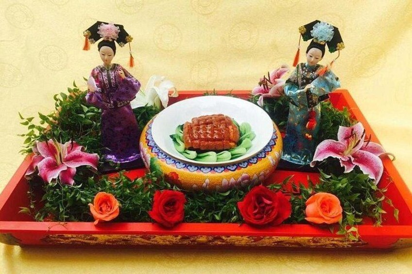 A traditional Chinese tray with two figurines, a plate of food, and decorative flowers. 1