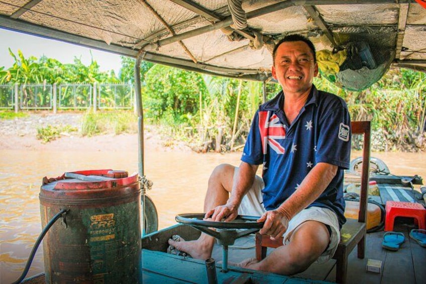 A person sitting on a boat, steering wheel in hand, with a fuel container and a fan visible. 5