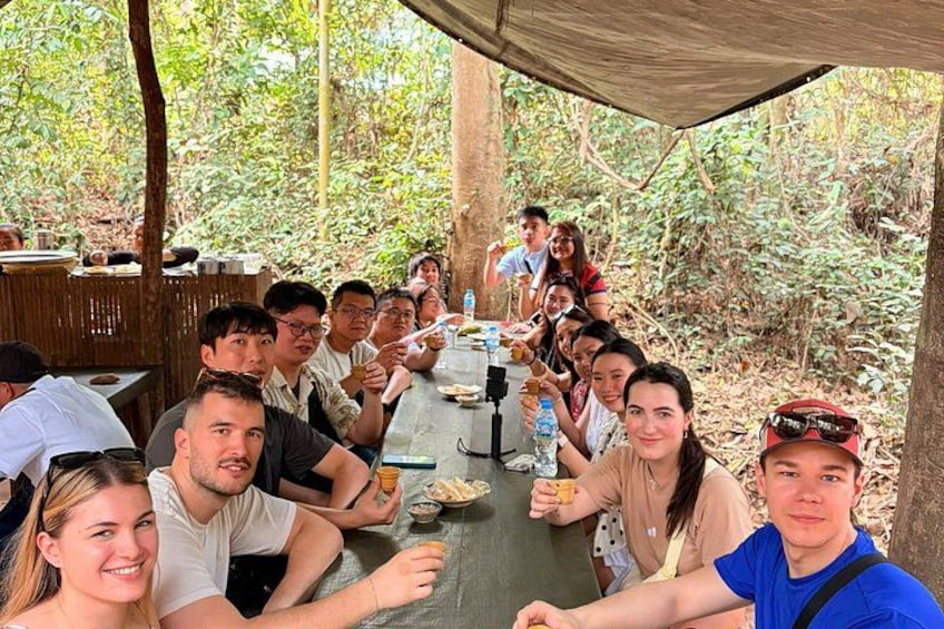 A group of people sitting at a table outdoors, surrounded by trees. 3