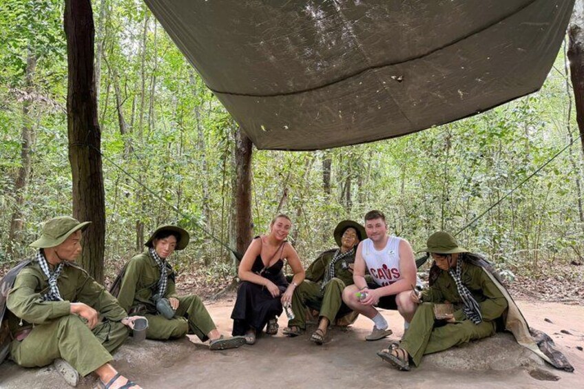 Un grupo de personas sentadas bajo una carpa en un bosque. 3