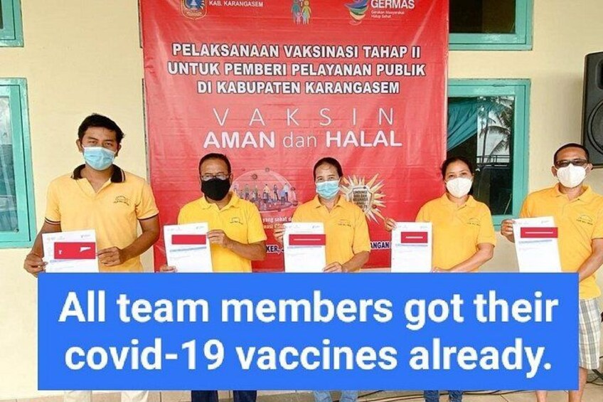 A group of people in yellow shirts holding vaccination certificates in front of a red banner with text in a non-English language. 2