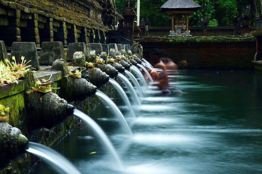 A water feature with multiple cascades, a person in the water, and traditional architecture in the background. 5
