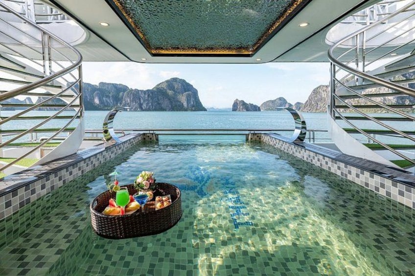Una piscina con una cesta flotante de bebidas y aperitivos, rodeada de una terraza con baldosas y vistas al mar y las montañas. 2
