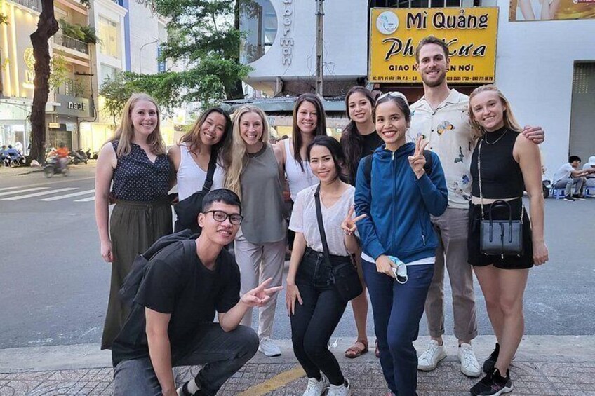 A group of people posing in front of a building with a sign that reads 'Mi Quang Phuc'. 2