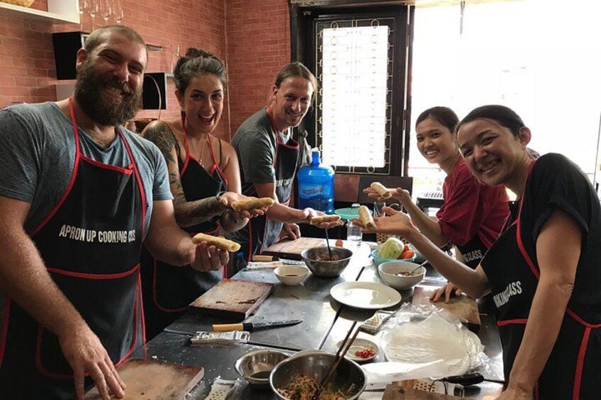 A group of people wearing aprons, preparing food in a kitchen with a brick wall and a window. 1