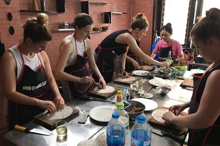 Personas preparando comida en una cocina, con delantales, tabla de cortar y diversos utensilios de cocina. 3