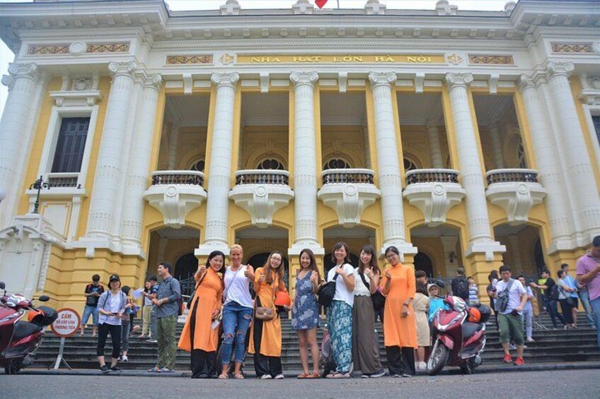 A group of people standing in front of a large, yellow building with columns and balconies. 3