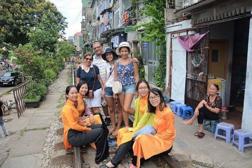 A group of people in orange clothing on a street with buildings and a parked car. 5