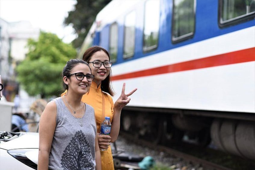 Two people standing next to a train with a red stripe. 4
