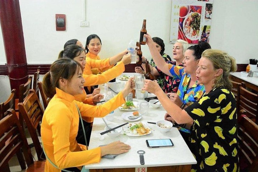 Un grupo de personas sentadas alrededor de una mesa, brindando con botellas. 5