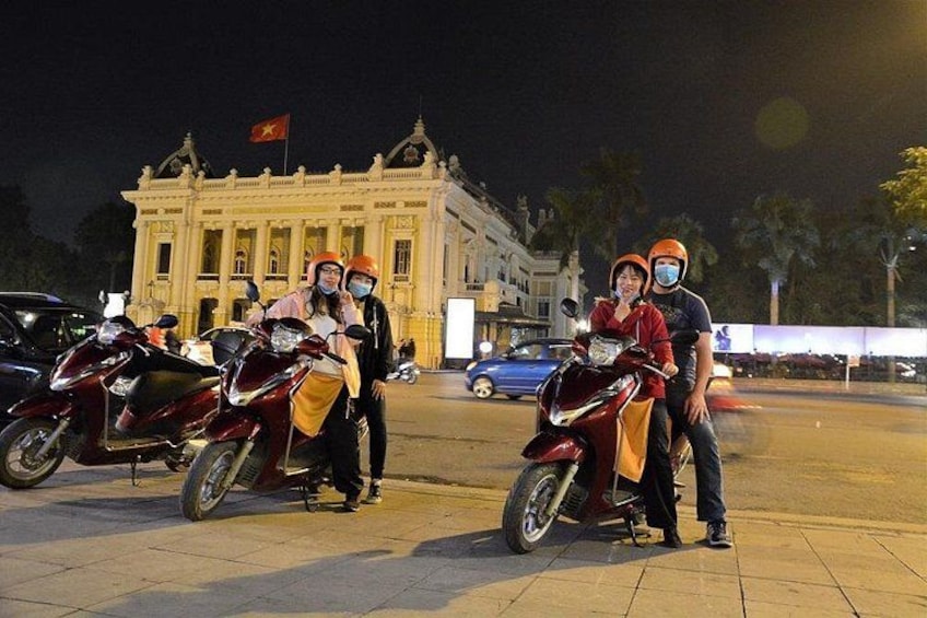 A group of people posing with motorcycles in front of a large building with a flag. 4