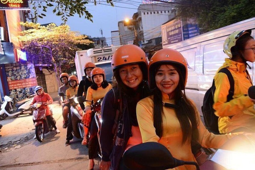 Un grupo de personas en motocicletas, con casco, en una calle con edificios y un autobús al fondo. 1