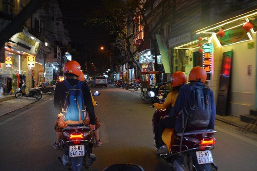 Dos motociclistas con cascos y mochilas circulando por una calle urbana de noche. 3