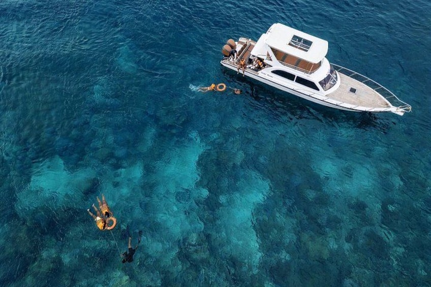 Eine Yacht liegt in klarem, blauem Wasser vor Anker, während sich eine Person in der Nähe aufhält. 3