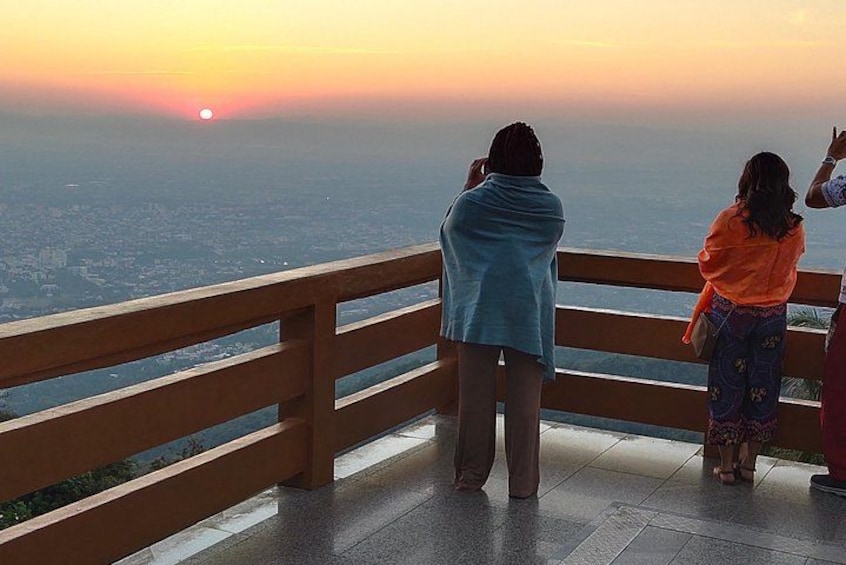 Two people standing on a balcony overlooking a cityscape during sunset. 2