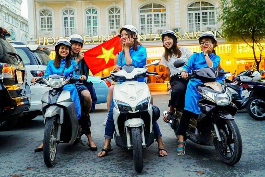 A group of people on scooters, a Vietnamese flag, and a building with 'HOTEL' signage. 1