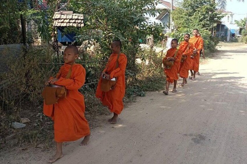 Monks in orange robes walking down a dirt road, carrying alms bowls. 5