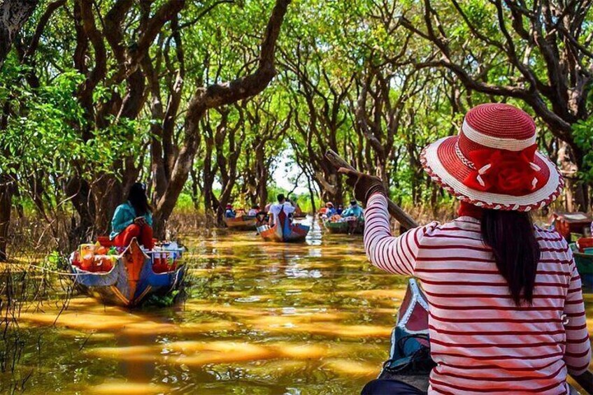 A person in a striped shirt and red hat paddling a boat through a waterway surrounded by trees. 2