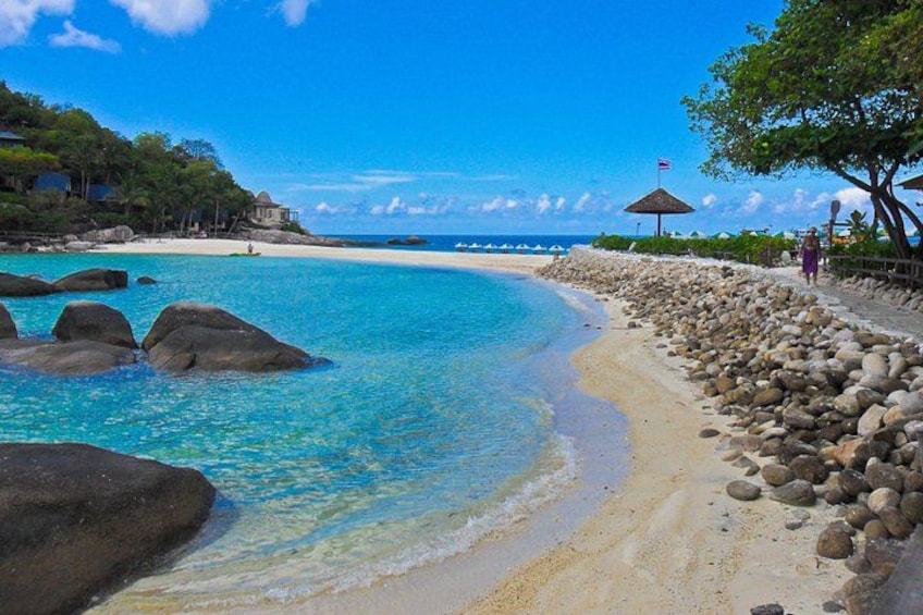 A beach with clear turquoise water, large rocks, a sandy shore, and a few trees. 5