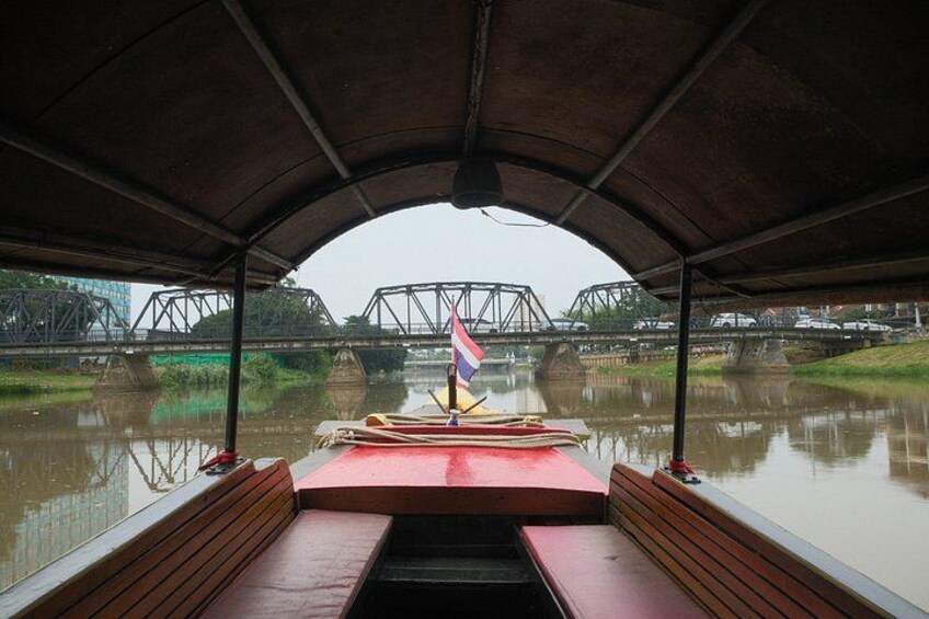 A covered boat with a flag, a bridge in the background, and calm water. 3