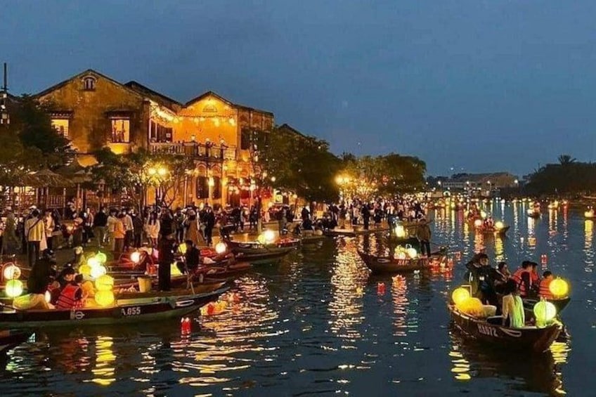 Ein Fluss mit Booten und Menschen, ein Gebäude mit Lichtern und eine Menschenmenge. 1
