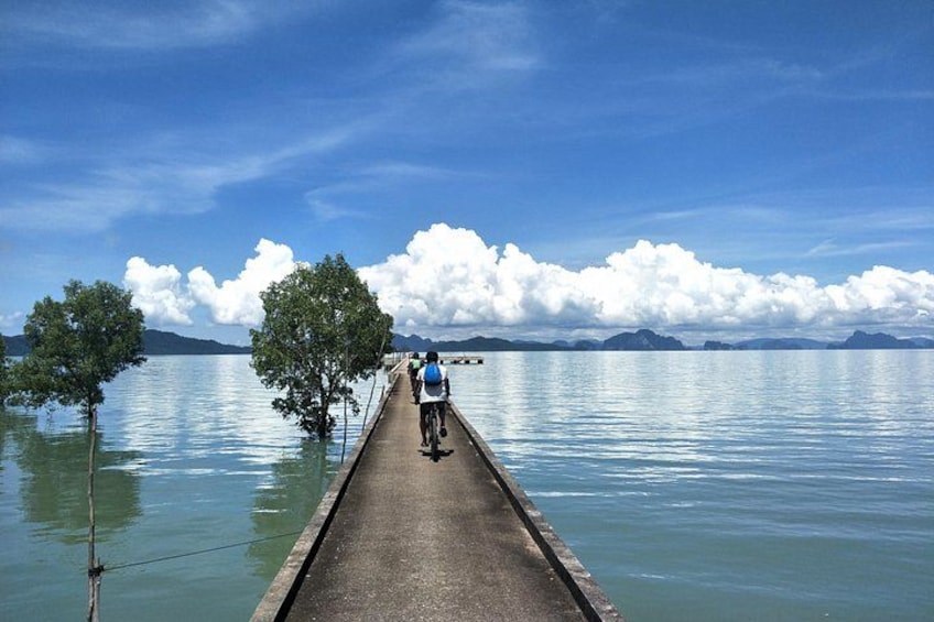 A person riding a bicycle on a narrow waterway surrounded by calm water and distant mountains. 4