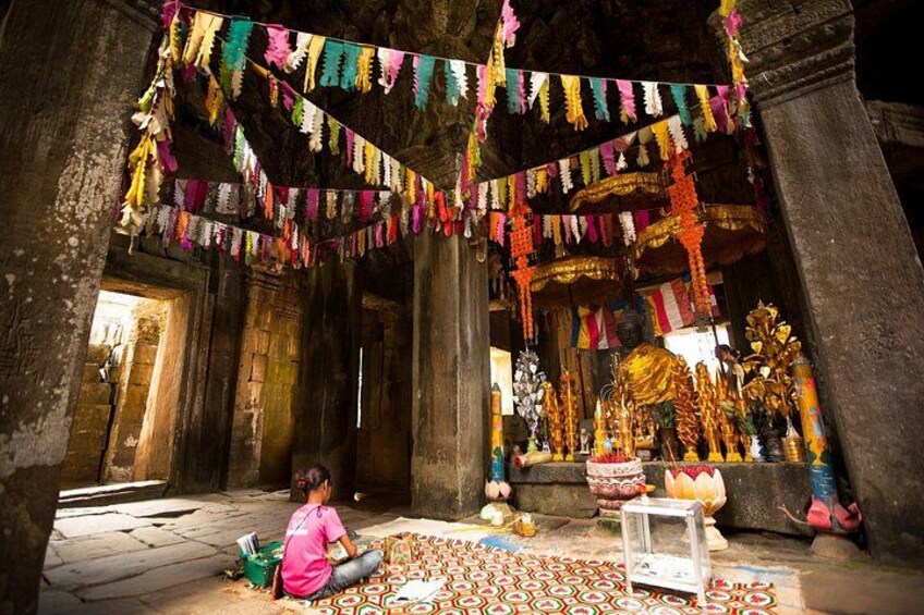 An ancient temple interior with colorful prayer flags, a seated person, and ornate statues. 2