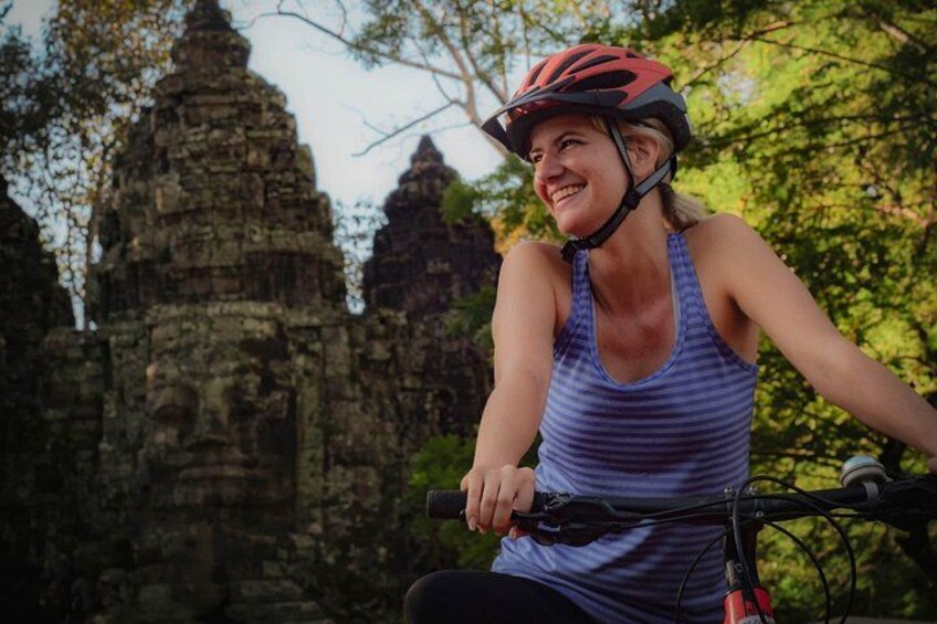 A person riding a bicycle with a helmet, in front of ancient stone structures. 1