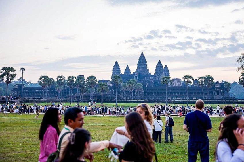A large crowd of people gathered in a grassy area with a historic temple in the background. 4