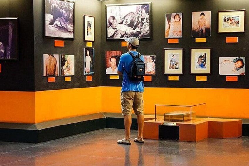 Eine Person steht in einem Ausstellungsraum mit Fotografien an den Wänden und Vitrinen. 3