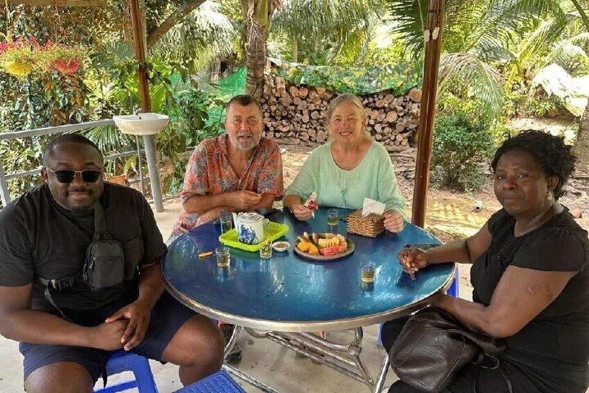Three people sitting at a round table outdoors with a tropical setting in the background. 2