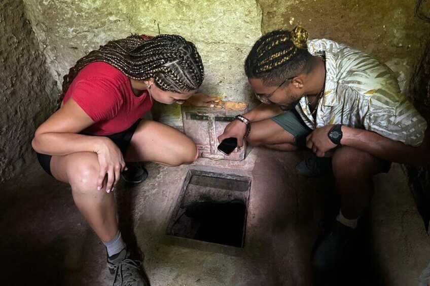 Two people examining a small, stone-built structure with a narrow opening. 5