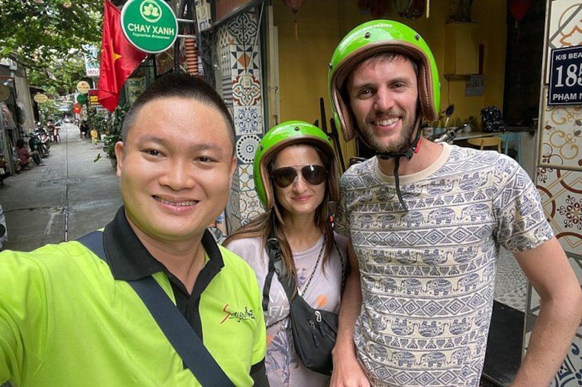 Trois personnes portant des casques, une rue bordée de boutiques et une enseigne sur laquelle on peut lire « CHAY XANH ». 4